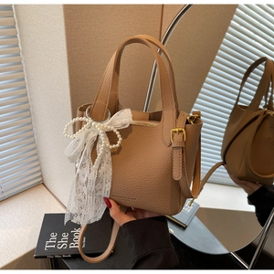Detail of khaki pebbled leather bucket bag with pearl lace charm and gold hardware