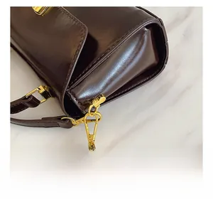 Close-up of golden lobster clasp hardware and dark brown glossy leather shoulder bag strap