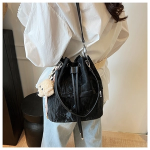 Detail of black drawstring bucket bag with textured fabric and plush puppy charm