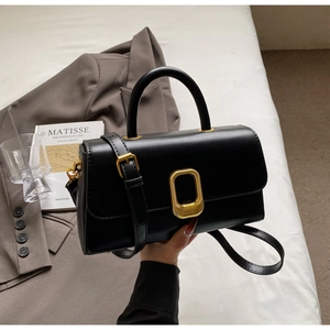 Détail d'un sac bandoulière minimaliste en cuir noir avec boucle dorée et poignée