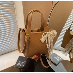 Detail of tan pebble leather bucket bag featuring a beaded lace bow and long strap
