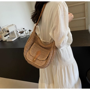Detail of hand-woven crescent straw bag with brown leather strap in a cafe setting