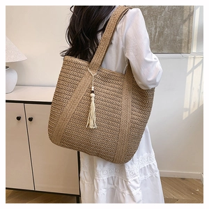 Detail of hand-woven straw tote bag with white tassel pendant and wide shoulder strap