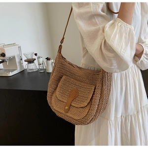 Straw hobo bag with brown leather details and front pocket shown in a cafe setting