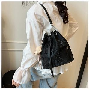 Detail of black drawstring bucket bag with textured pleats and cute beige bear charm