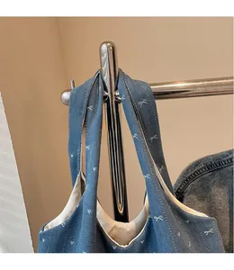 Detail of blue denim tote bag with white bow embroidery hanging on a metal hanger