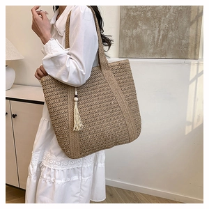 Detail of a large straw tote bag with white tassel on shoulder of a female model