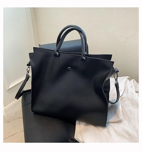 Detail view of large black leather tote bag with round metal buckle and sturdy dual handles