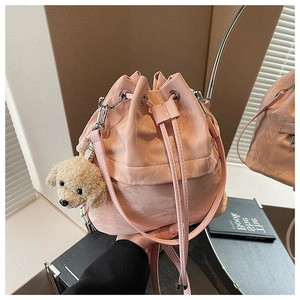 Pink drawstring bucket bag with plush dog charm on a reflective table surface
