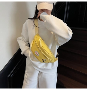 Dettaglio di un borsello giallo in nylon con ricamo indossato da una modella in bianco