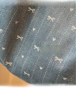 Detail of light blue denim fabric with white bow and heart jacquard pattern on a tote bag