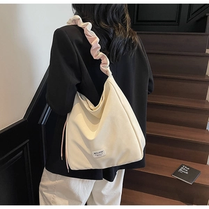 Detail of a beige canvas tote bag with unique ruched shoulder strap and brand logo
