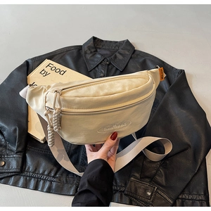 Close-up of cream canvas chest bag with embroidery and woven zipper on a leather jacket