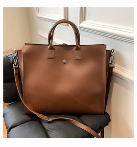 Detail view of brown leather tote bag with silver hardware on a quilted seat