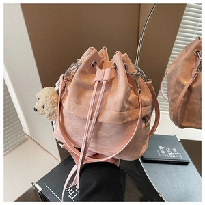 Macro detail of a pink pleated drawstring bucket bag with a plush dog charm and silver metal hardware
