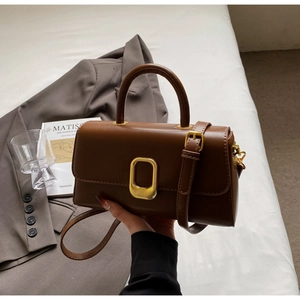 Détail d'un sac à main marron caramel avec boucle dorée et bandoulière sur tissu blanc
