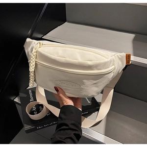 Detail of off-white canvas chest bag featuring brand embossing and orange woven label