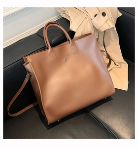 Top view of brown faux leather tote bag on black leather sofa with trench coat detail
