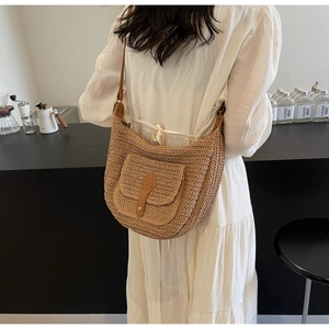 Detail view of woven straw shoulder bag with leather buckle and slim strap on model