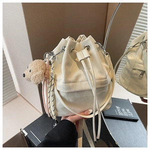 Detail of cream drawstring bucket bag with cute plush puppy charm and metal buckle