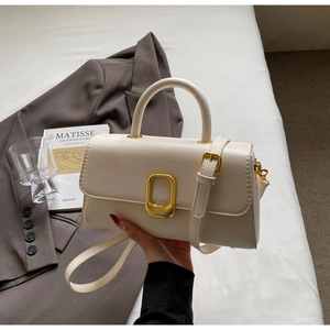 Gros plan d'un sac à main minimaliste crème avec boucle dorée et bandoulière en cuir