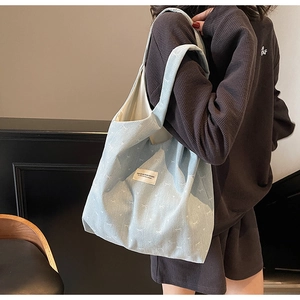 Detail of light blue denim tote bag with white bow patterns and branded woven label