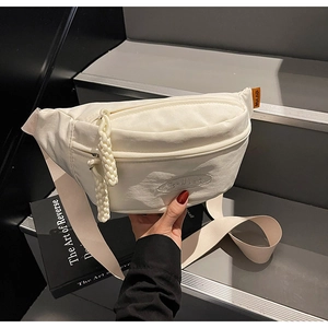 Detail of white canvas crossbody bag with orange logo tag and thick woven zipper pulls