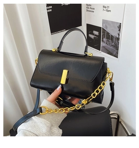 Detail of black glossy leather crossbody bag with gold metallic clasp and chain strap