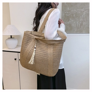 Detail of handwoven straw tote bag with wide handles and a white tassel decorative charm