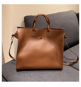 Detail of a dark brown leather tote bag with adjustable strap on a grey sofa