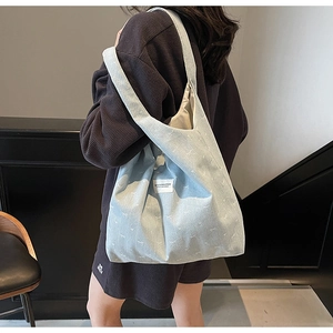 Detail view of light blue denim tote bag with white bow embroidery on a model