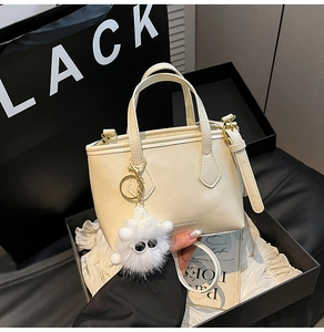 Détail du sac seau crème avec logo doré et bijou de sac en peluche dans un coffret cadeau
