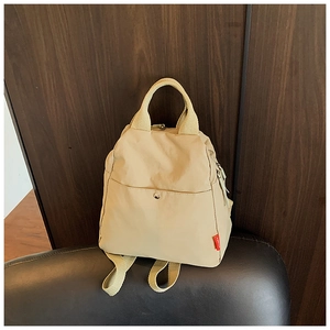 Detail view of beige nylon backpack with top handle and metal snap front pocket