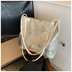 Detailed close-up of elegant cream jacquard bucket bag with blue floral embroidery and tassel