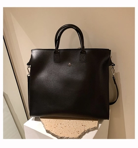 Detail of a black leather tote bag with vintage silver metal button on a stone pedestal