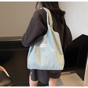 Detail view of large light blue denim tote bag with white bow pattern and brand label
