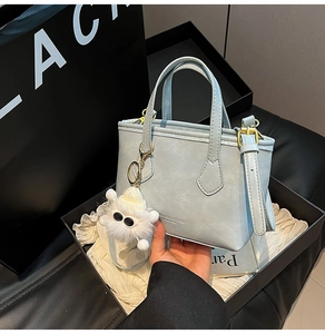 Détail d'un sac seau bleu clair avec finitions dorées et breloque en peluche blanche