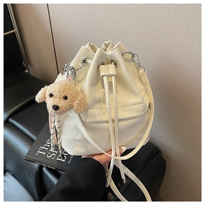 Close-up of white drawstring bucket bag with shiny finish and teddy dog charm accessory