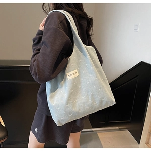 Close-up of light blue denim tote bag with white bow prints and patch on model's shoulder