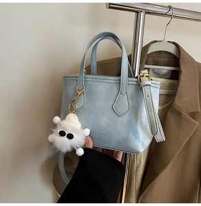 Detail of light blue leather bucket bag with a cute monster plush charm on a hanger