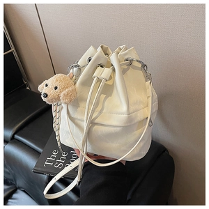 Detail view of white drawstring bucket bag with silver hardware and plush dog pendant