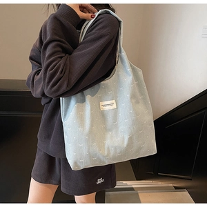 Detail of light blue denim tote bag with white bow embroidery and branded label