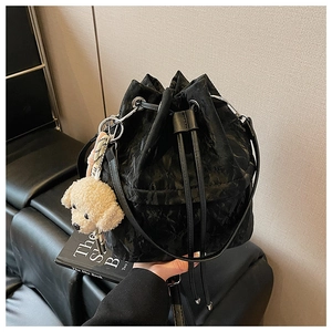 Detail of black drawstring bucket bag featuring crinkled texture and dog plush pendant