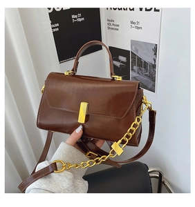 Detail of dark brown glossy leather handbag featuring elegant gold metal twist lock and chain