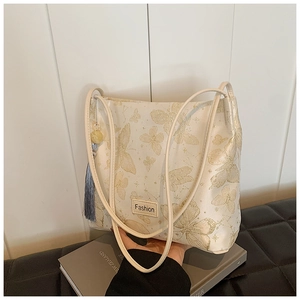 Detail of white bucket bag with gold butterfly prints, blue tassel, and fashion label