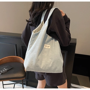 Detail of light blue denim tote bag with bow embroidery and branded studio label