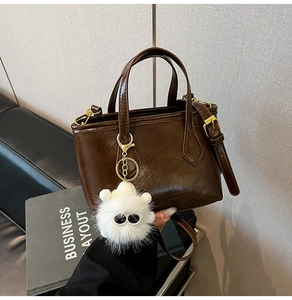 Détail du sac seau en cuir marron foncé avec un charmant monstre en peluche blanc
