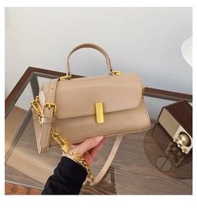 Detail of apricot square handbag featuring gold rectangle buckle and chain strap