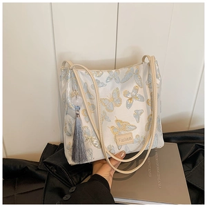 Close-up of butterfly embroidery and tassel charm on a cream white bucket bag