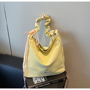 Detail of light yellow tote with pleated handles and decorative pink cords on a fashion book